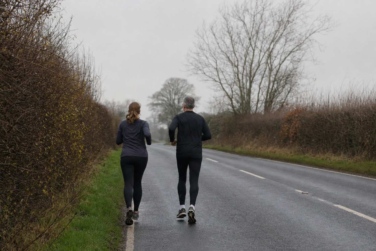 Two recreational runners running steadily away along an open road on a grey morning