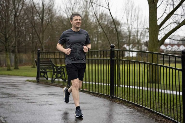 A man running an easy pace along a tarmac park loop on an overcast morning