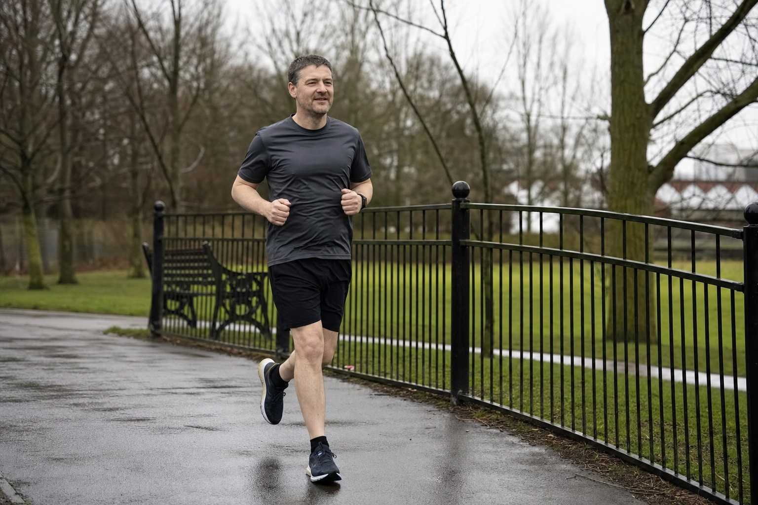 A man running an easy pace along a tarmac park loop on an overcast morning