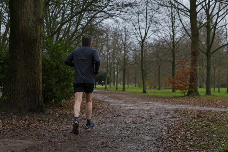 A man running away along a wooded parkland trail on a grey day
