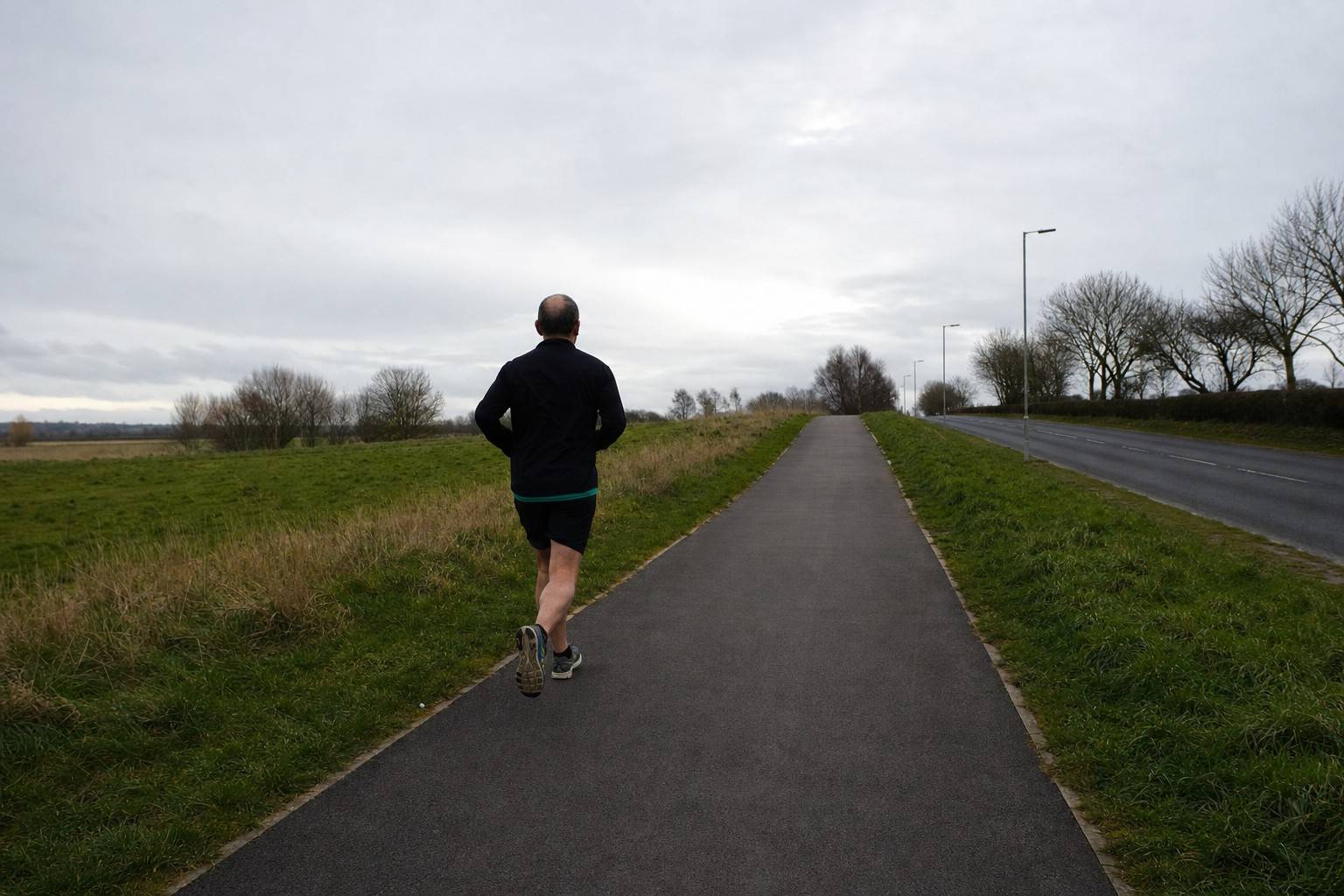 A runner heading along an open path on a grey morning, with the way stretching ahead