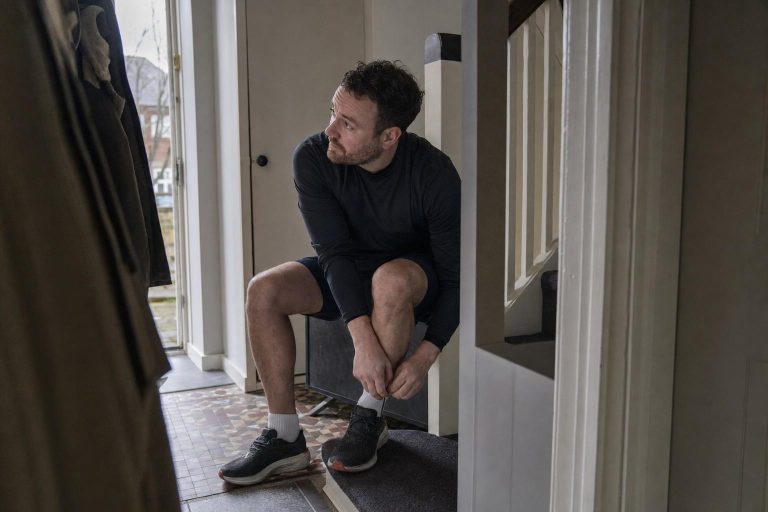A man lacing his running shoes in the hallway on a grey morning before heading out