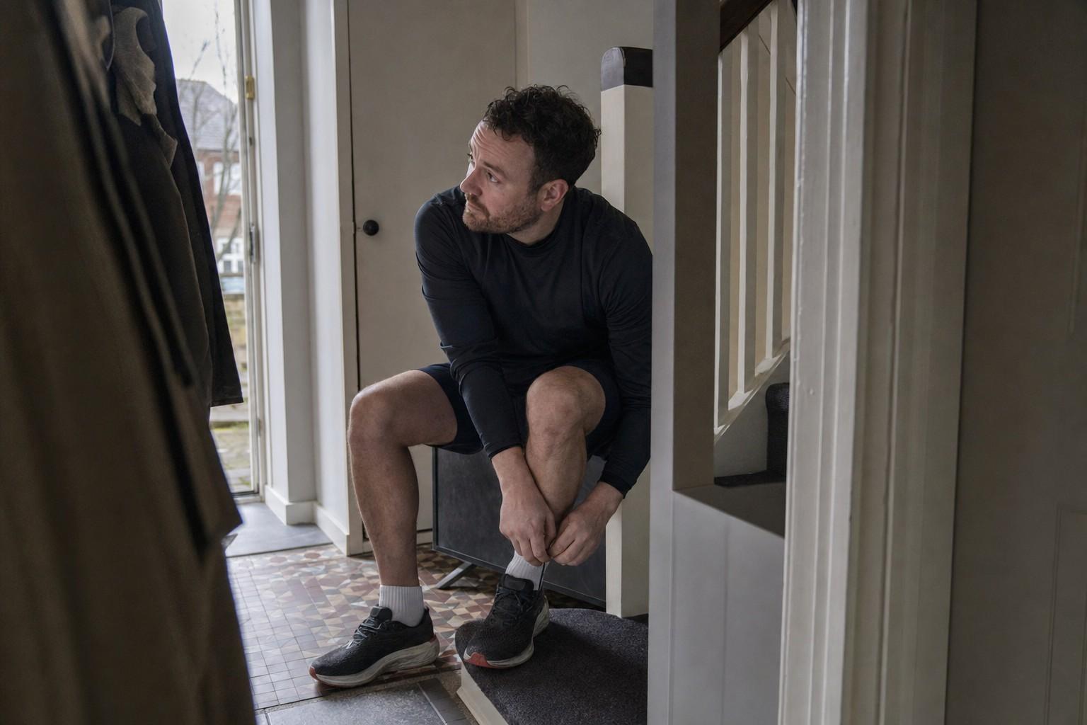 A man lacing his running shoes in the hallway on a grey morning before heading out