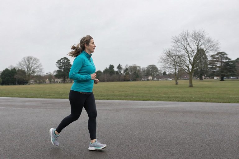 A woman jogging at an easy pace along a wide open path in a bright running top