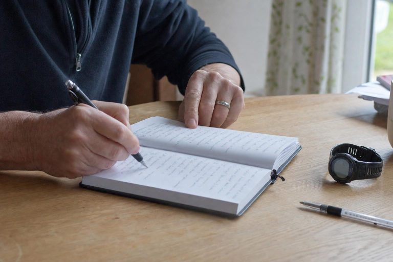 A close side view of hands writing in a training log at a desk